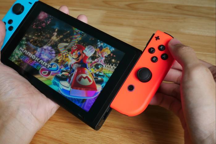 A handheld gaming console is cradled in the palm of a hand while a component is detached from the side