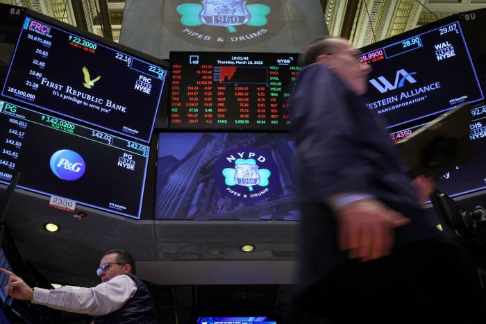 Traders at the NYSE walk in front of screens showing First Republic Bank stock